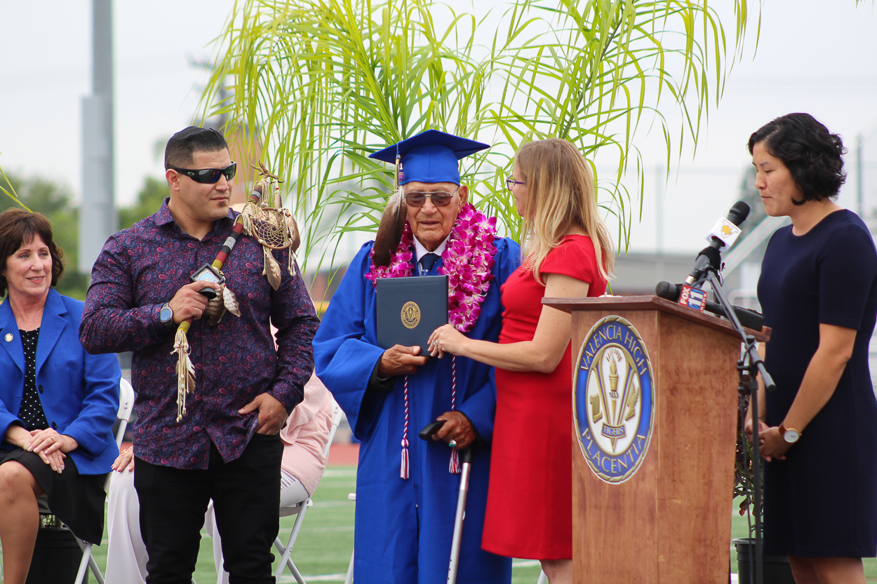 Upon the stage at the 50 yard line in Bradford Stadium, Mr. Filiberto Lopez Montano receives high long-awaited high school diploma from Board President, Carrie Buck, and Valencia High School Principal, Olivia Yaung on Friday, June 7, 2019.