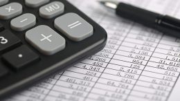A calculator and a ball pen is on a balance sheet. Concept for sales, profit and cost.