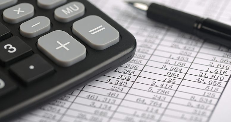 A calculator and a ball pen is on a balance sheet. Concept for sales, profit and cost.